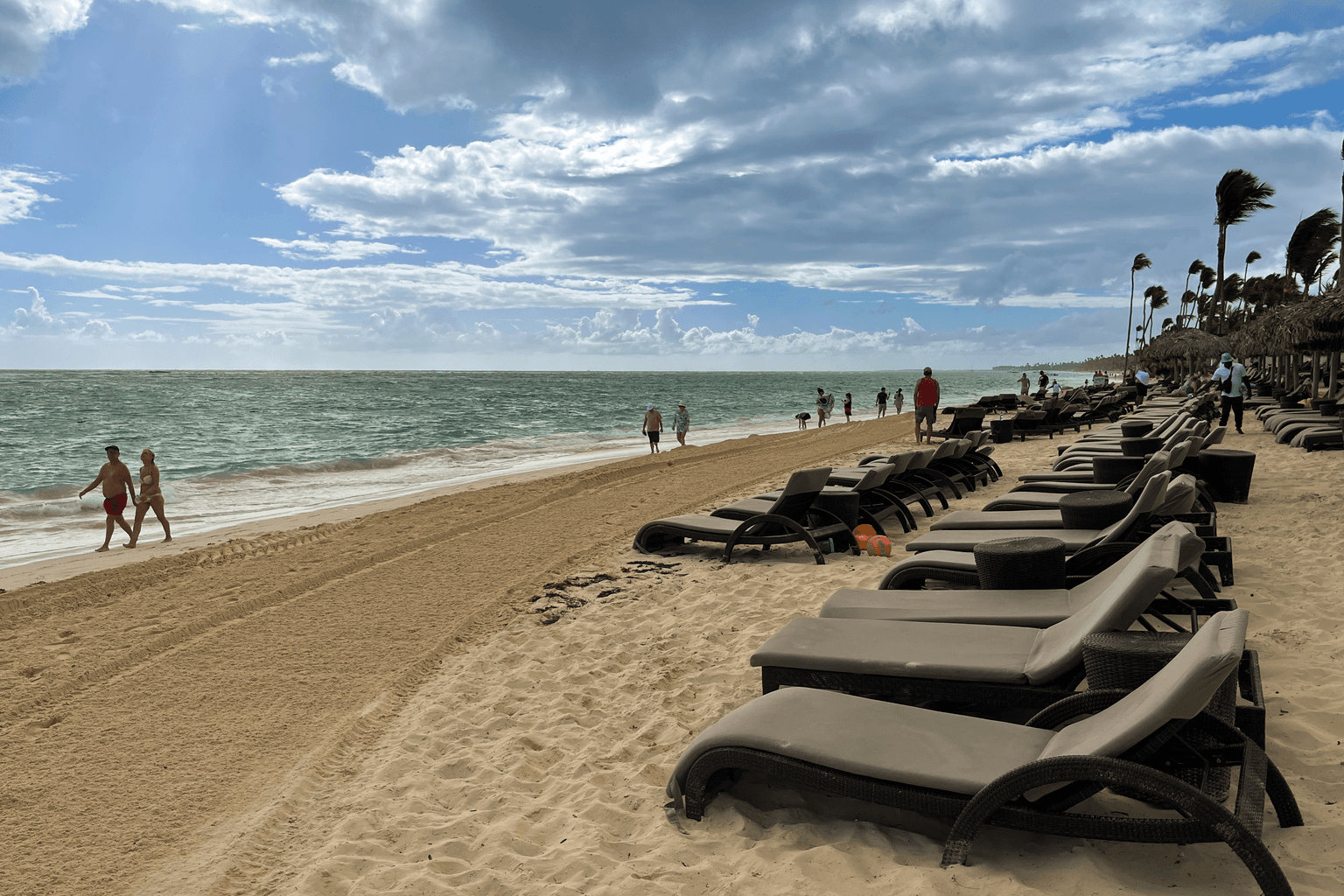 Bávaro Beach in Punta Cana with white sand, turquoise water, resort loungers, palm trees and beachgoers along the shoreline.