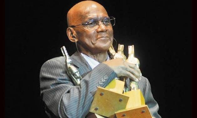 Cuco Valoy posing with a display of trophies and awards.